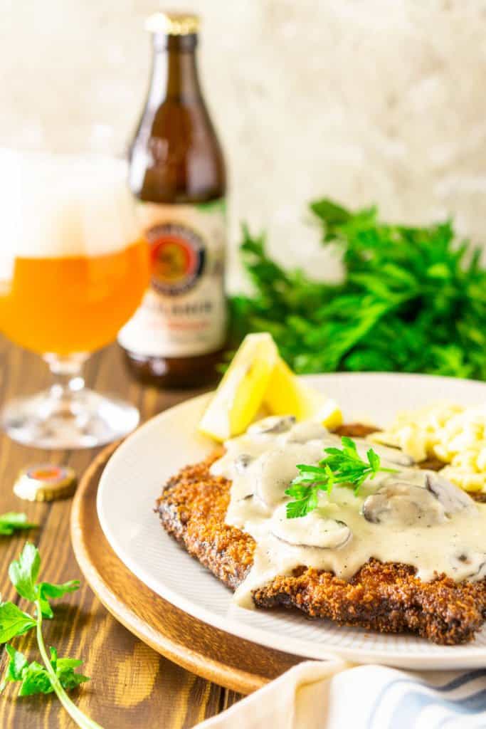 The beer-brined schnitzel topped with creamy mushroom gravy with a bunch of fresh parsley and a hefeweizen in the background.