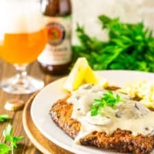 The beer-brined schnitzel topped with creamy mushroom gravy with a bunch of fresh parsley and a hefeweizen in the background.