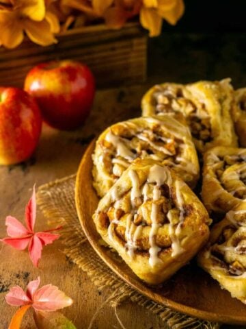 Looking down on a plate of apple cinnamon rolls with apples and leaves to the side.