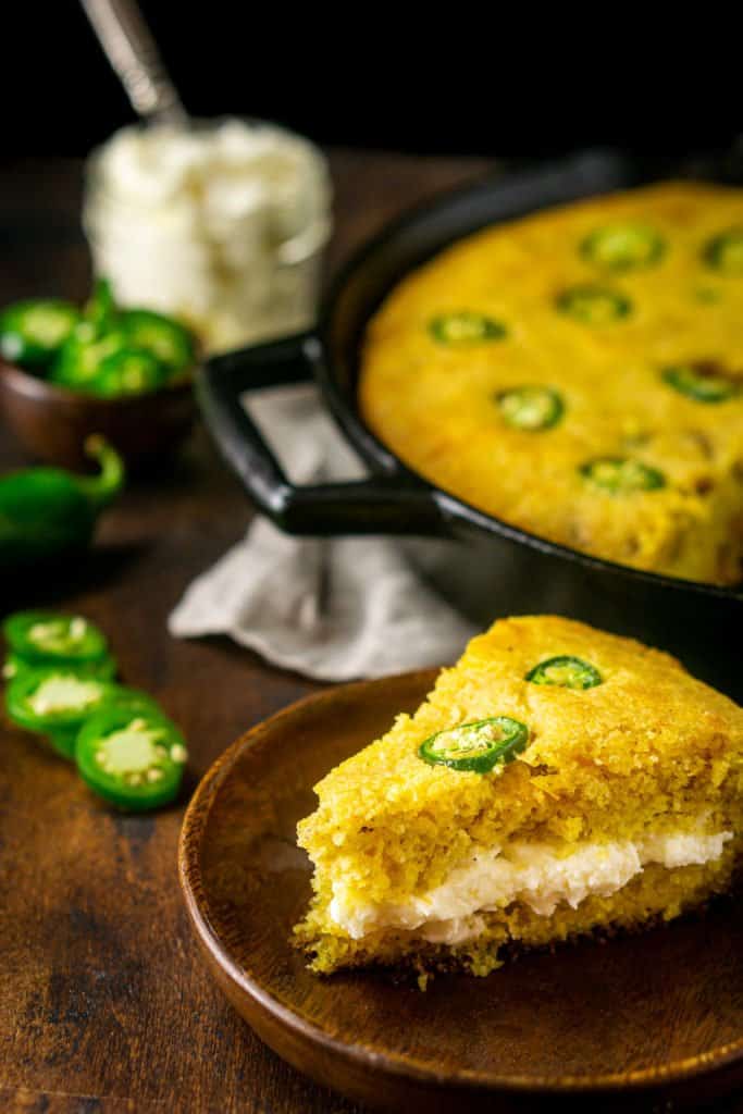 A slice of the jalapeno popper cornbread filled with the whipped cream cheese butter on a small wooden plate.