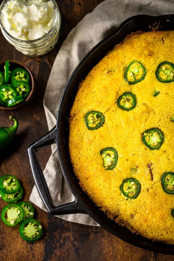 An aerial view of the skillet of jalapeno popper cornbread with jalapeno slices on the side.