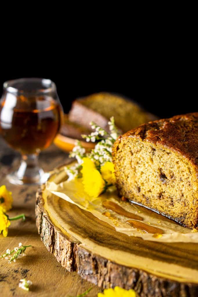 The maple-bourbon banana bread on a wooden platter with flowers to the side.
