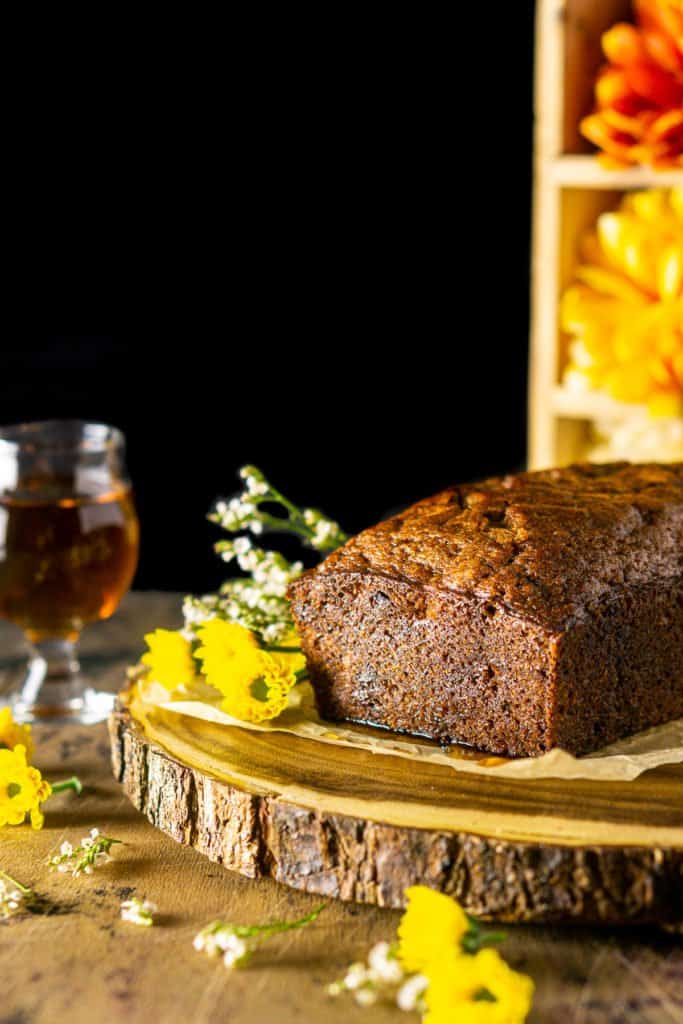 The banana bread before it's been sliced on a wooden platter with flowers all over.