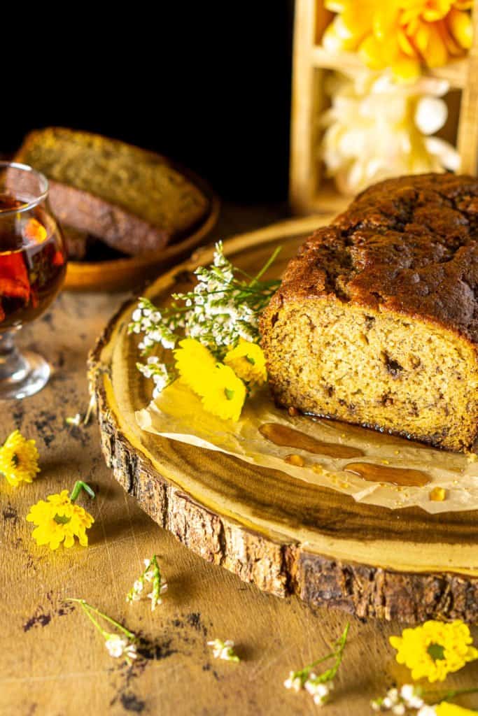 Looking down on a loaf of boozy banana bread on a wooden platter with drops of maple syrup.