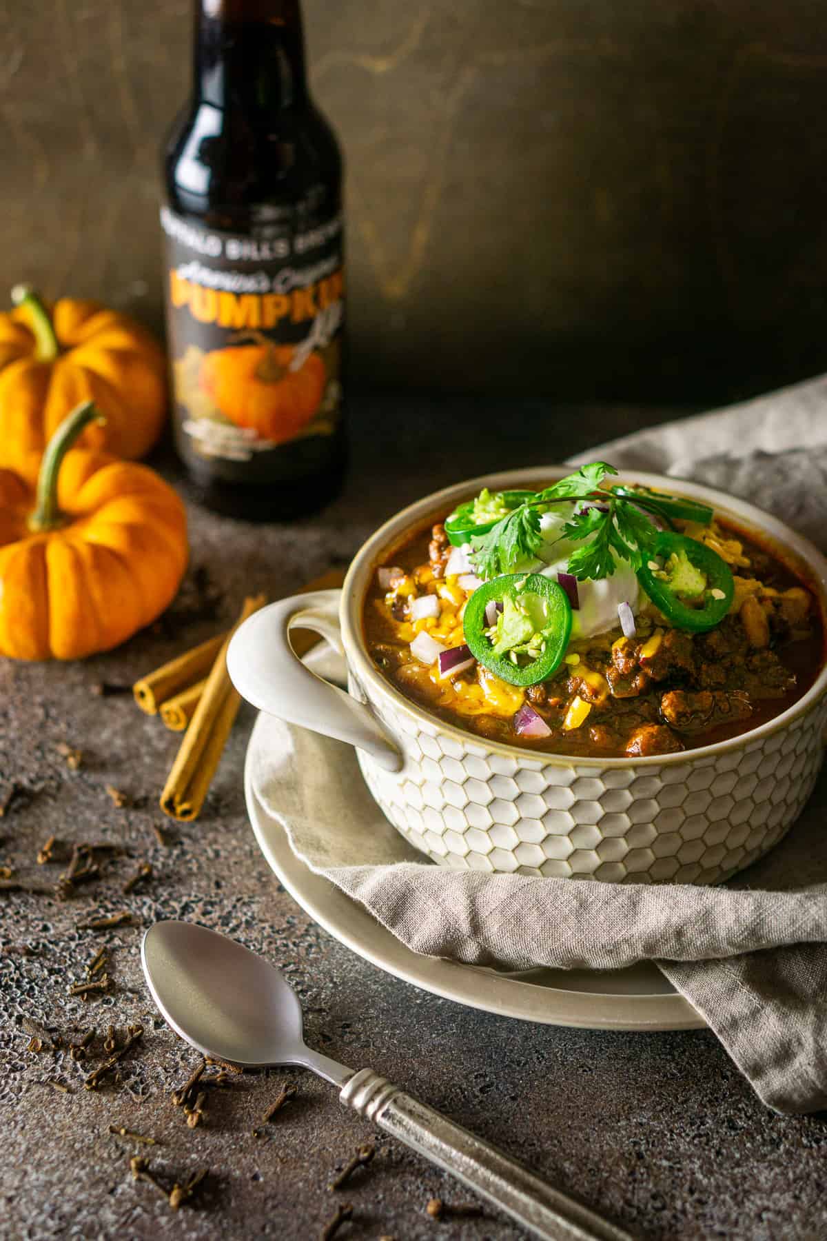 Looking down onto a bowl of pumpkin and chorizo chili with pumpkins to the left.