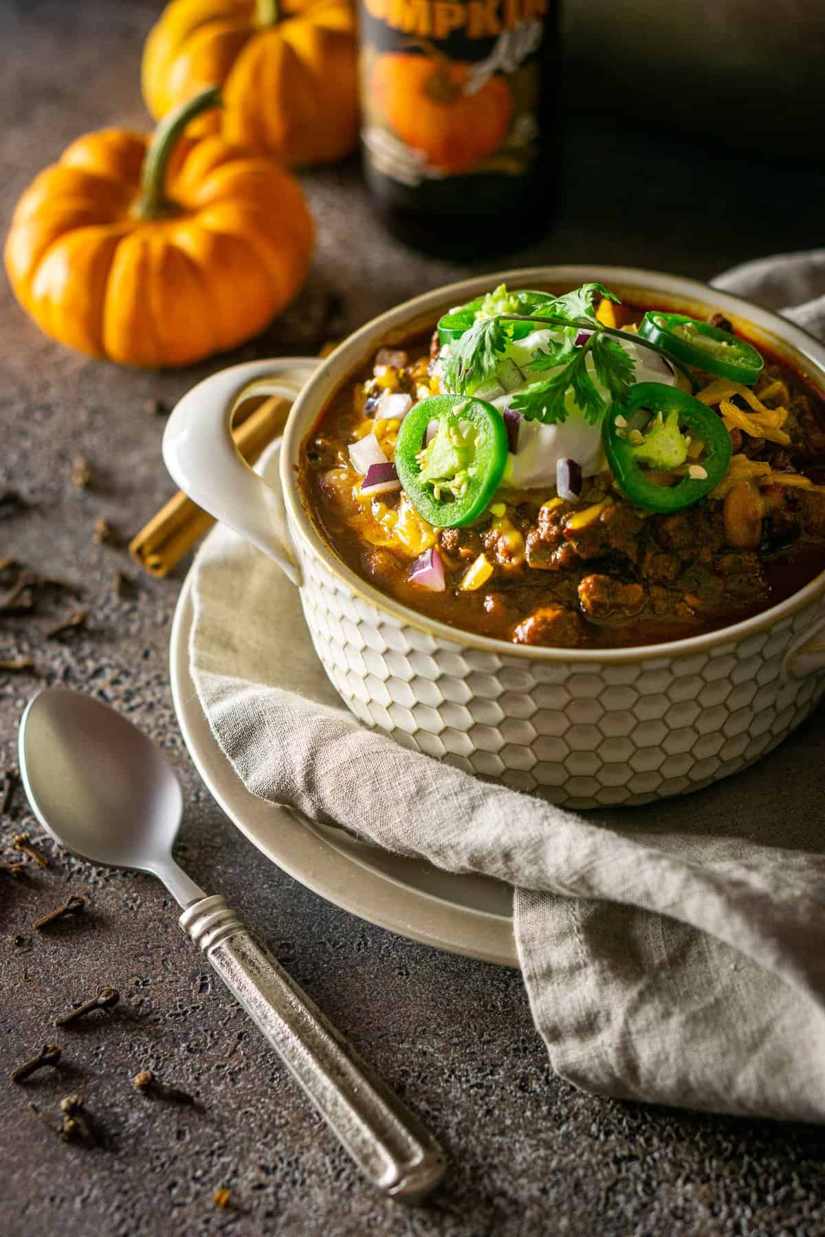 The pumpkin and chorizo chili on a plate with a spoon to the side and whole cloves surrounding it.