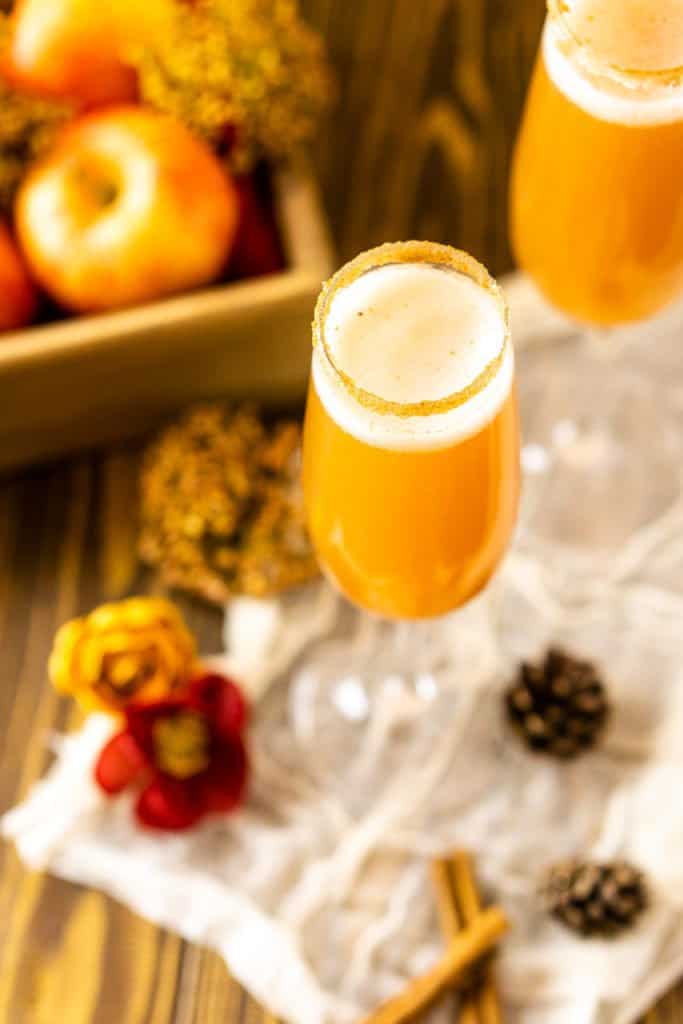 An aerial view of an apple Bellini with cinnamon sticks, pinecones and fall flowers to the side.