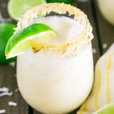 A coconut margarita with a yellow napkin and lime slices on the side with toasted coconut scattered around it.