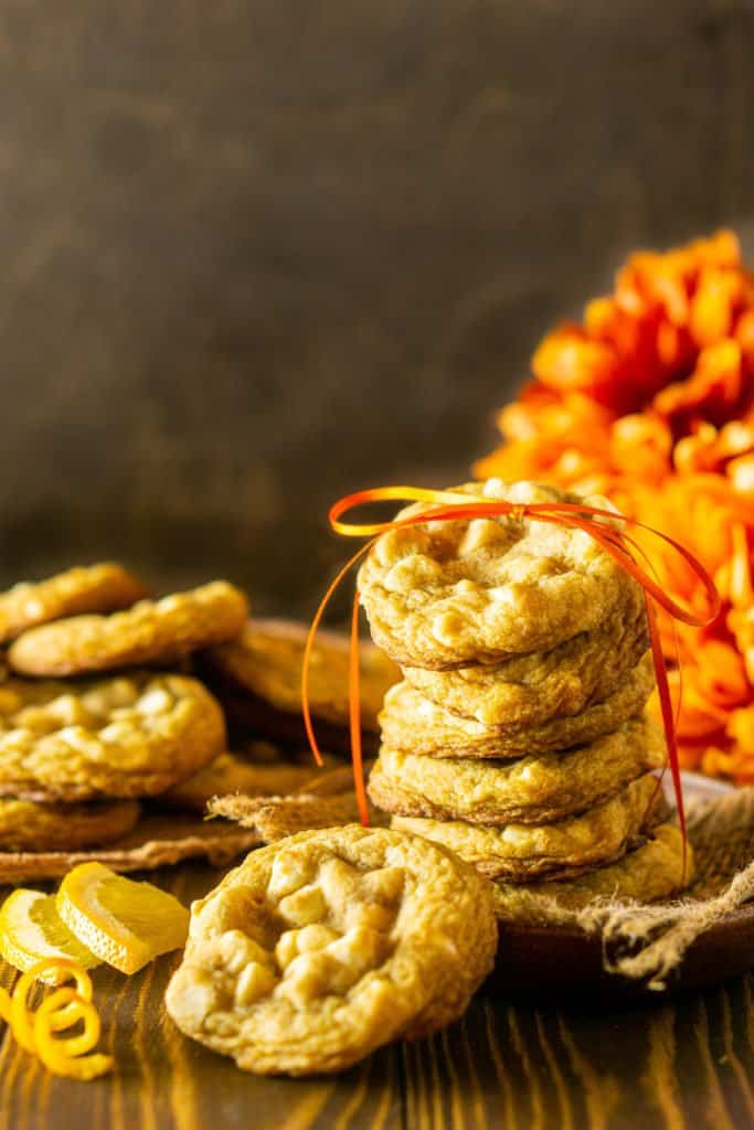 A stack of ginger-maple cookies with orange zest tied with a ribbon and orange flowers in the background.