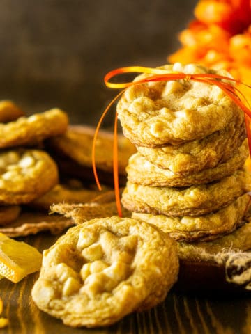 A stack of ginger-maple cookies with orange zest tied with a ribbon and orange flowers in the background.