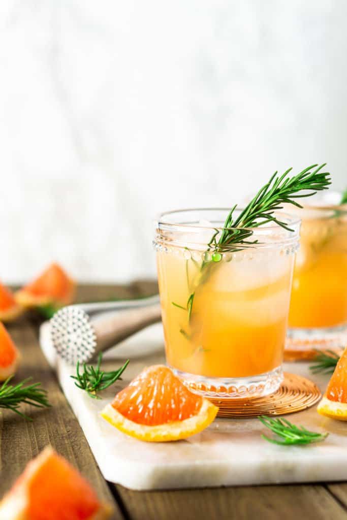 Two rosemary-grapefruit spritzers with a white marble background. 