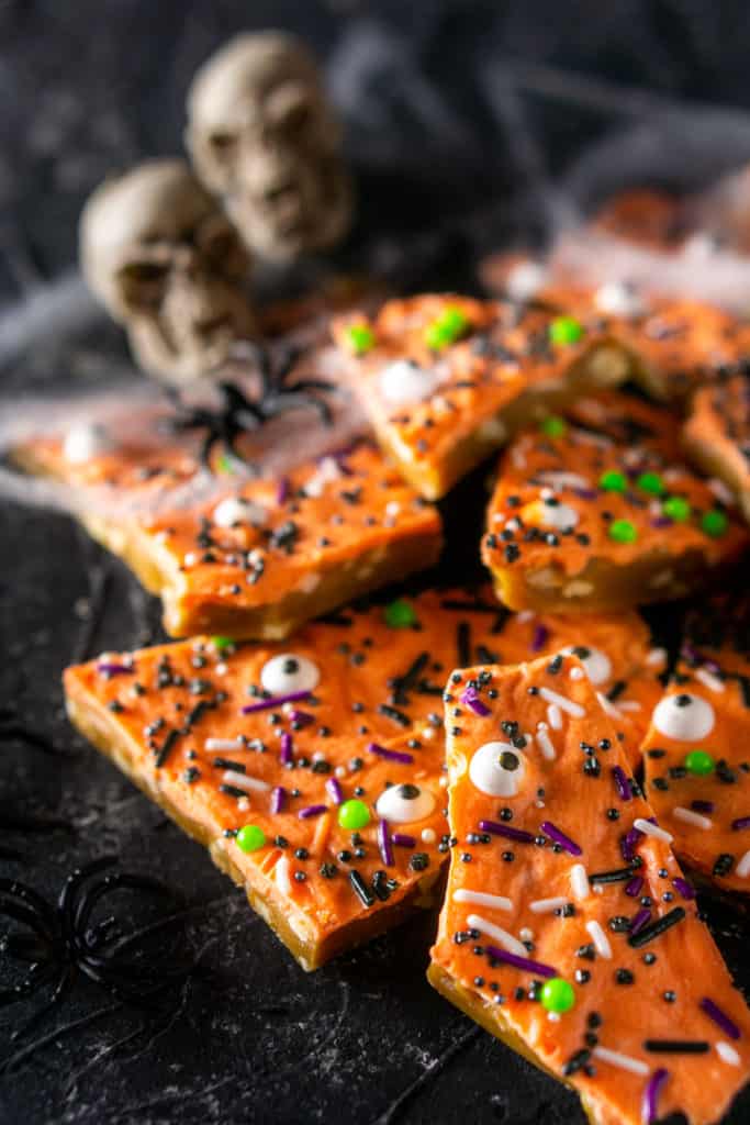 A pile of Halloween toffee with spider webs, plastic spiders and skulls in the background.