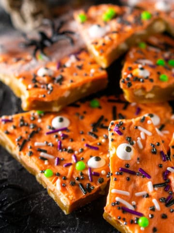 A pile of Halloween toffee with spider webs, plastic spiders and skulls in the background.
