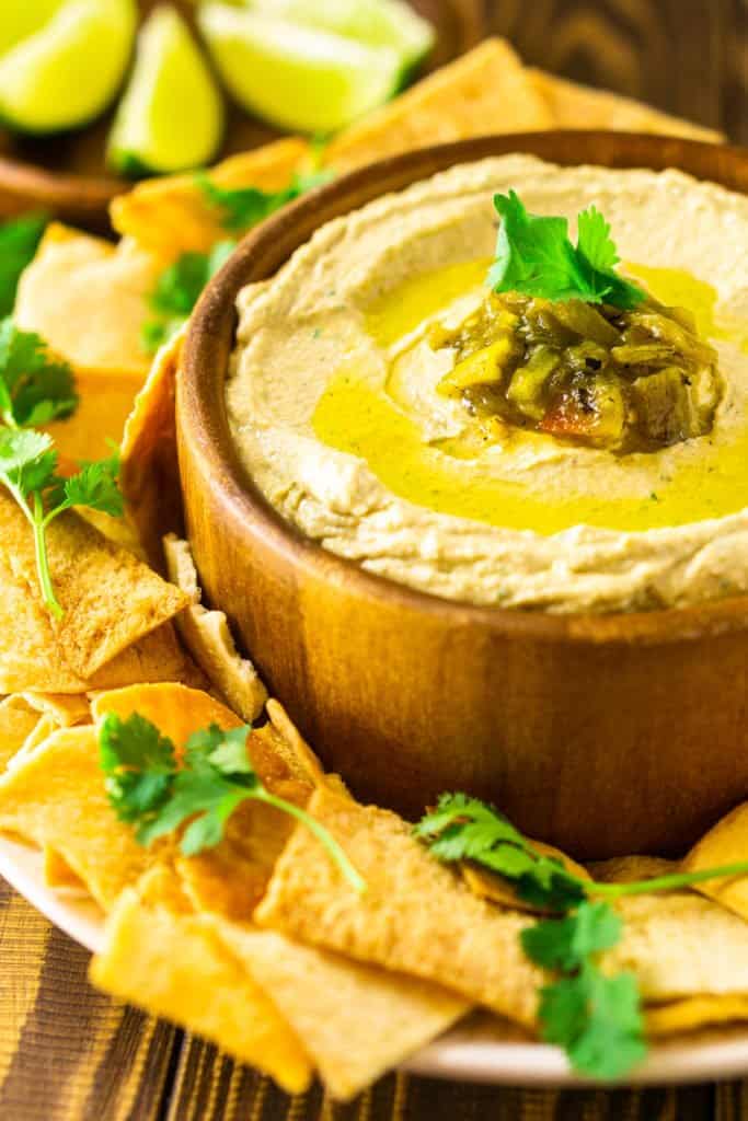 A close-up shot of the Hatch green chile hummus in a wooden bowl with pita chips surrounding it.