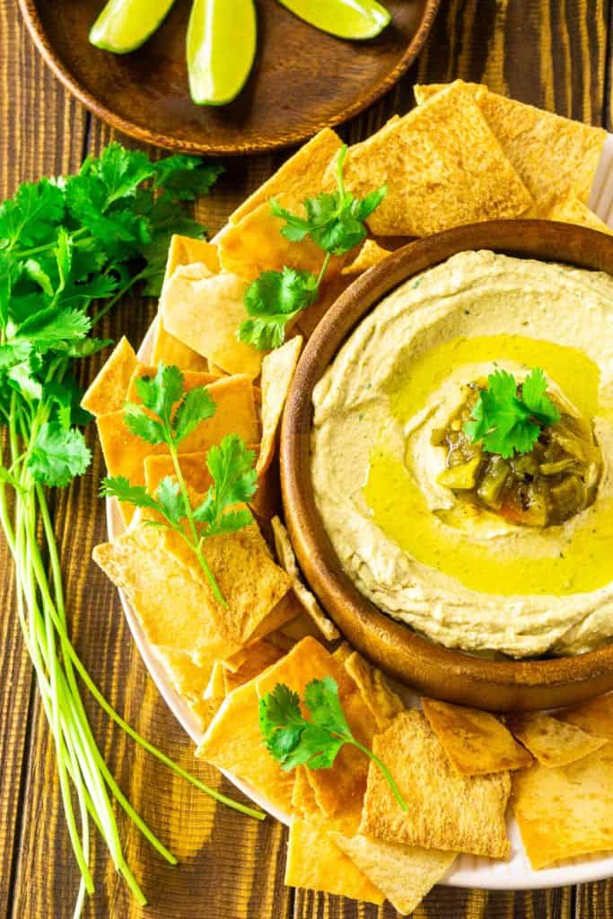 An aerial view of the Hatch green chile hummus in a wooden bowl with cilantro on the side.