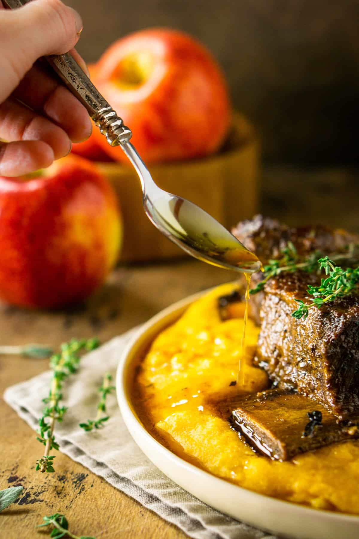 Pouring a spoonful of the sauce onto the polenta and apple cider short ribs.