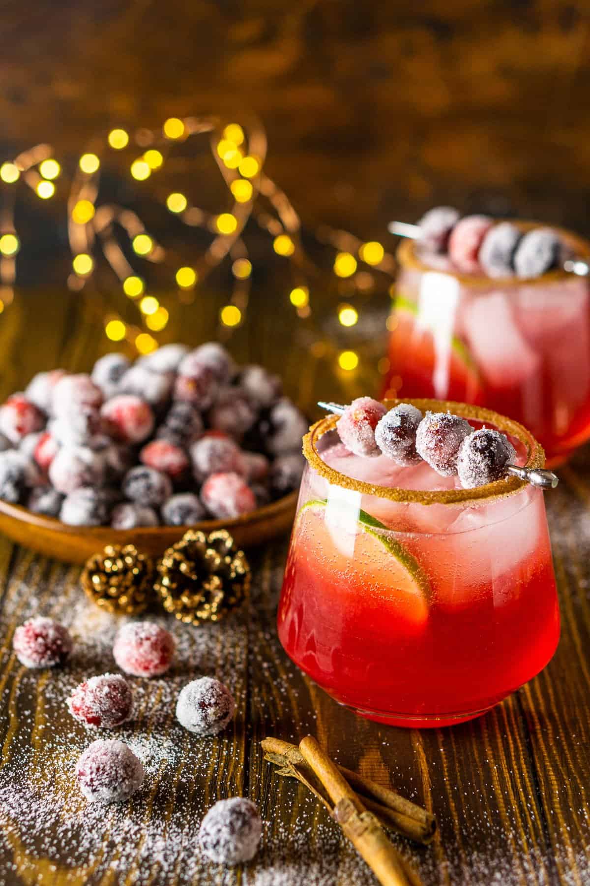 Two sparkling cranberry-ginger margaritas with a plate of sugared cranberries on a white plate to the side.