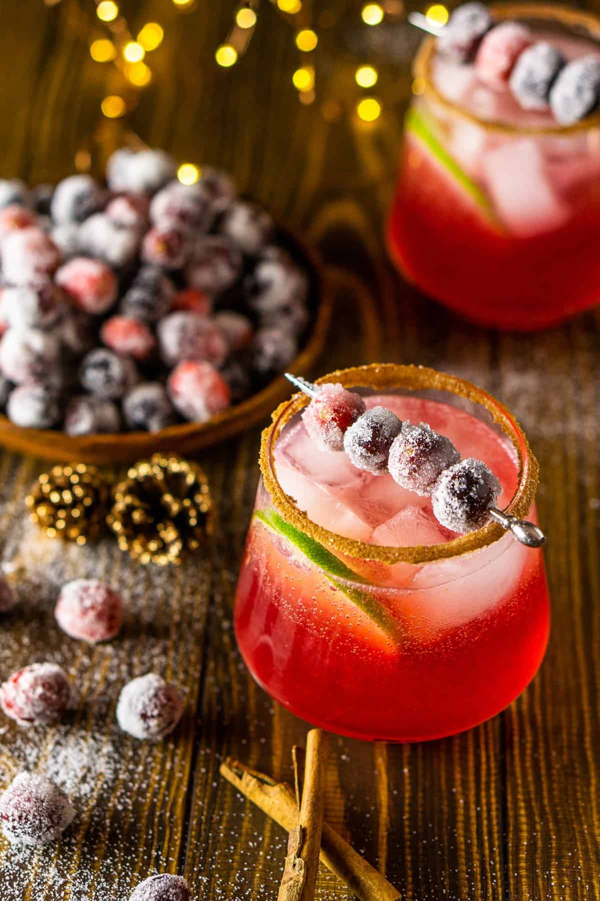 A sparkling cranberry margarita with lights and sugared cranberries on the side.