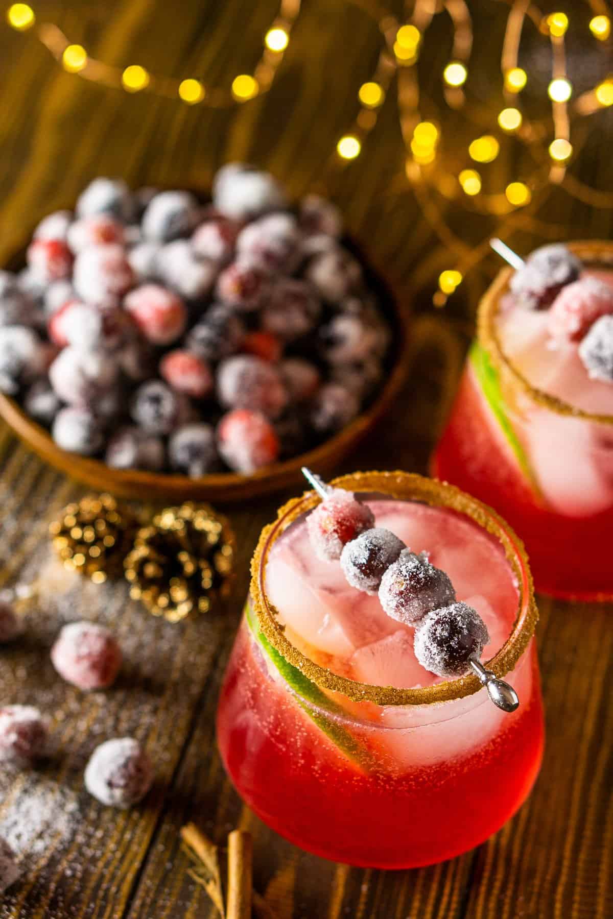 An aerial view of two sparkling cranberry-ginger margaritas with sugared cranberries behind them.