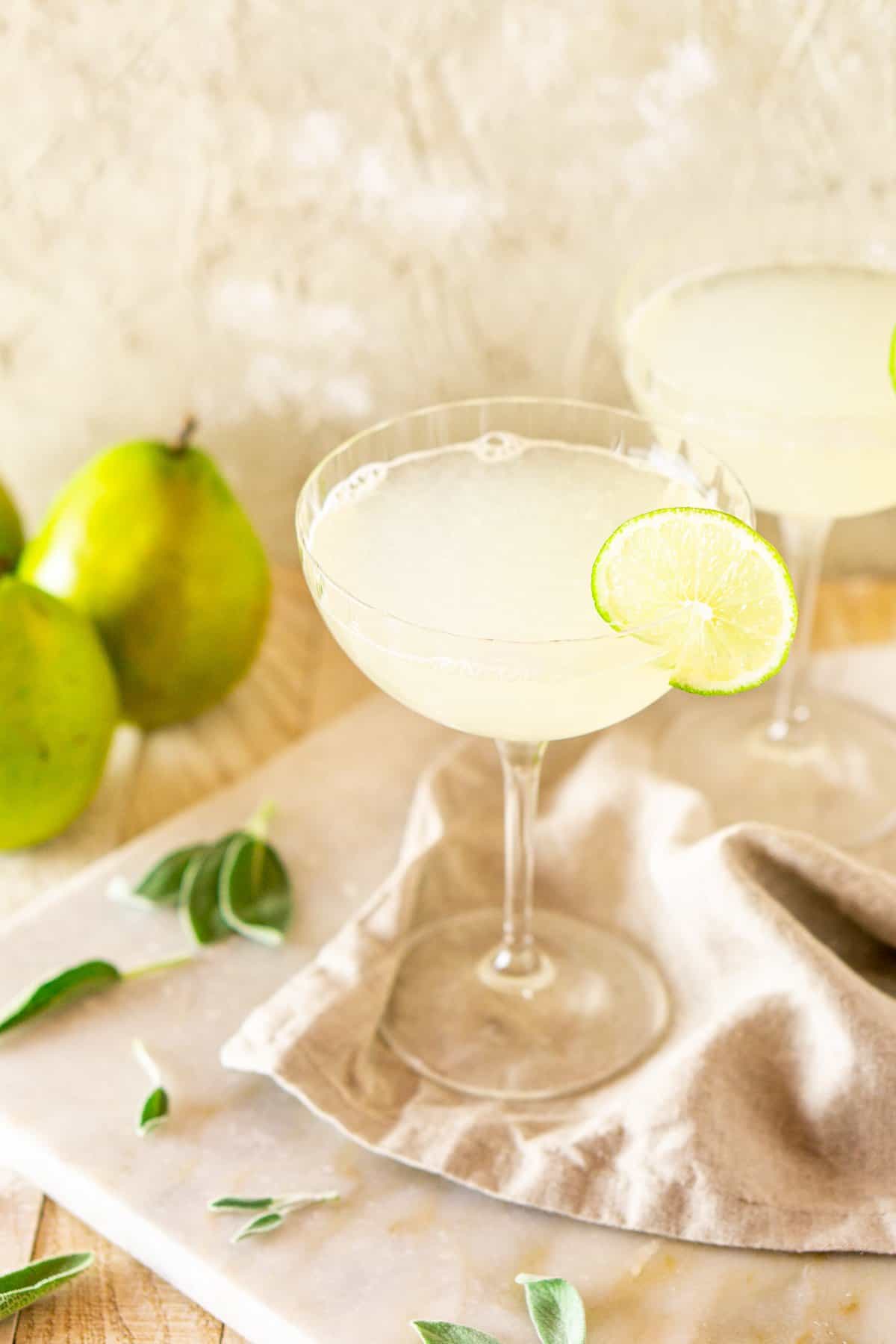 A close-up shot of the gimlet with pears to the side on a white marble board.