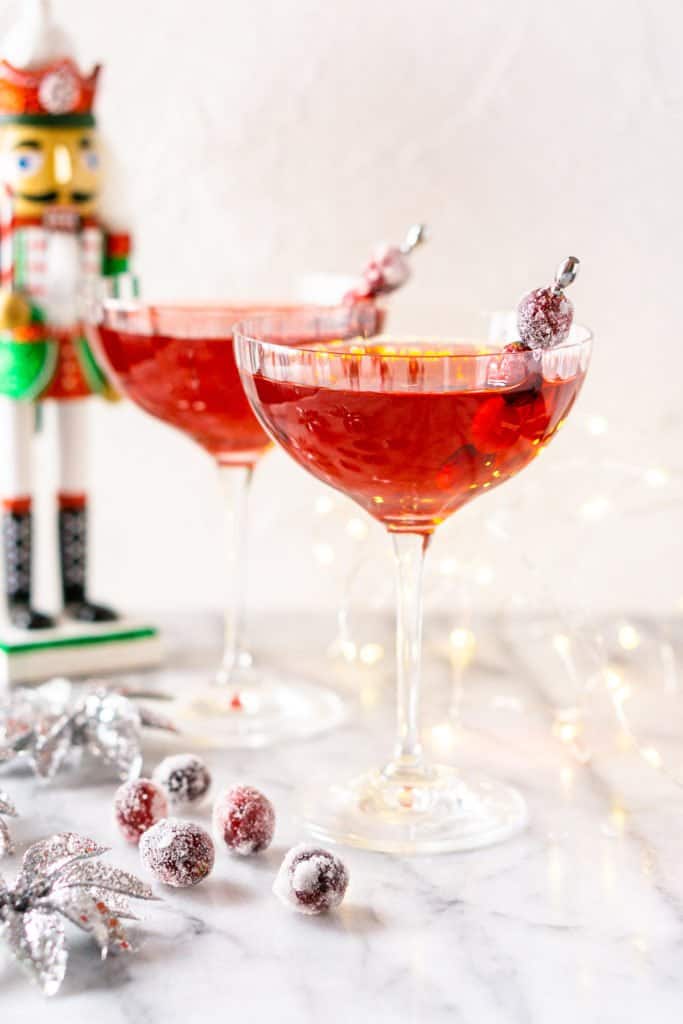Two Sugar Plum Fairy Martinis on a marble board with a nutcracker and lights behind them.