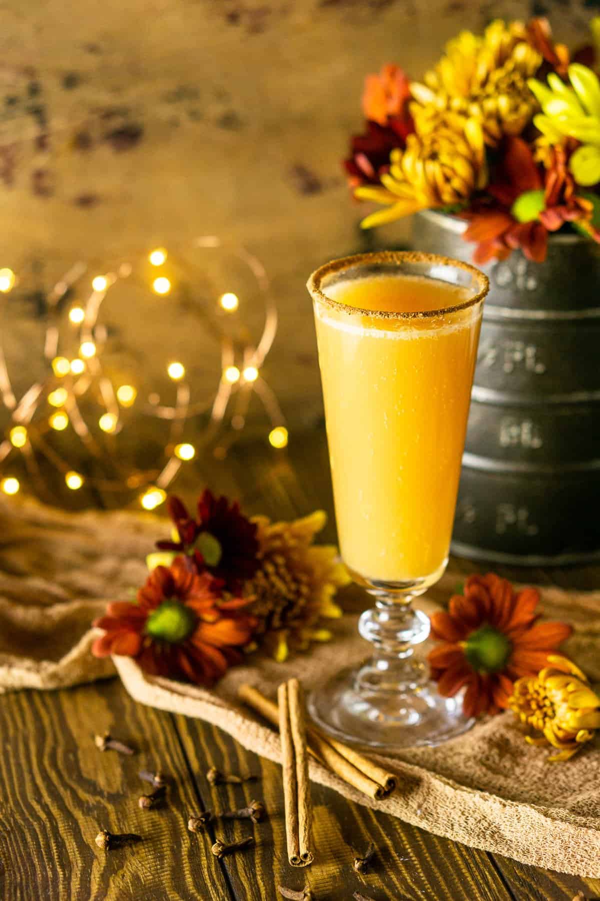 A single Thanksgiving mimosa in front of fall flowers with lights to the side.