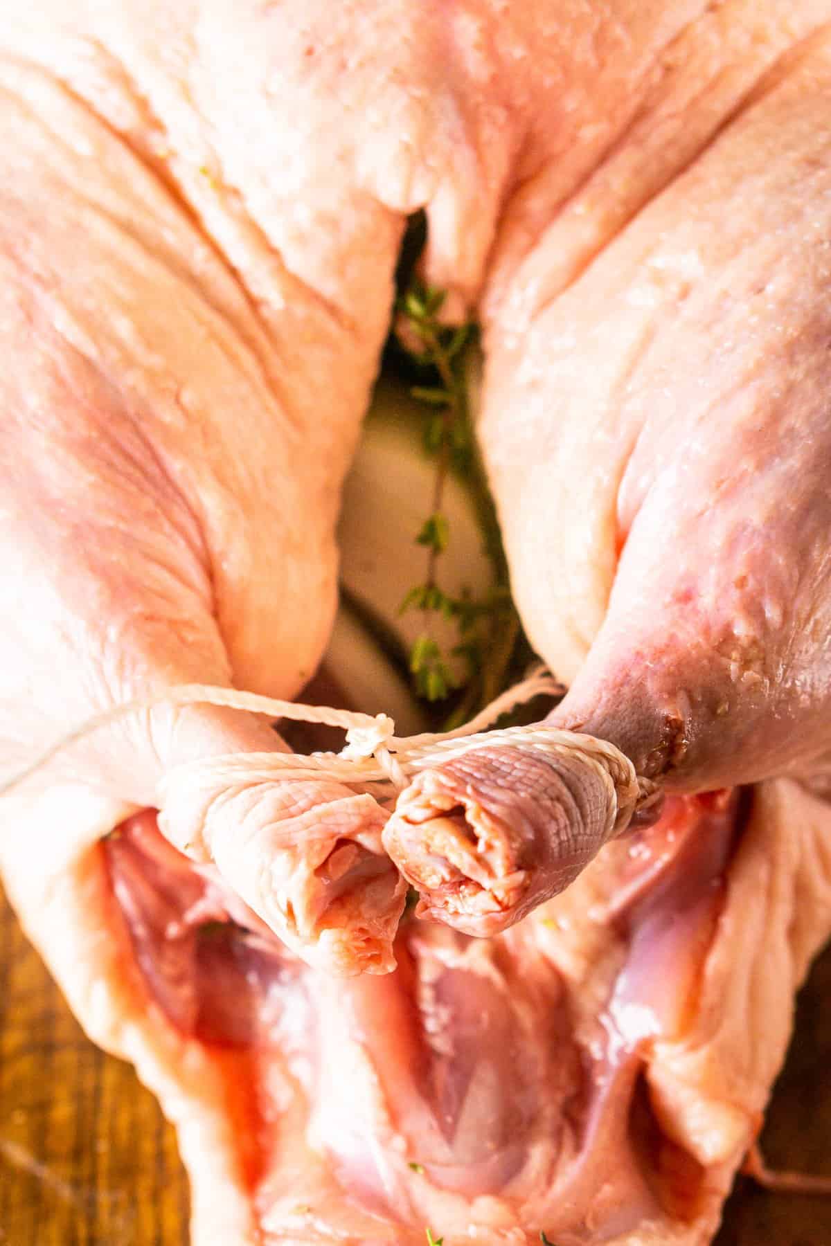 Stuffing the bird with the aromatics and tying the legs together on a wooden cutting board.