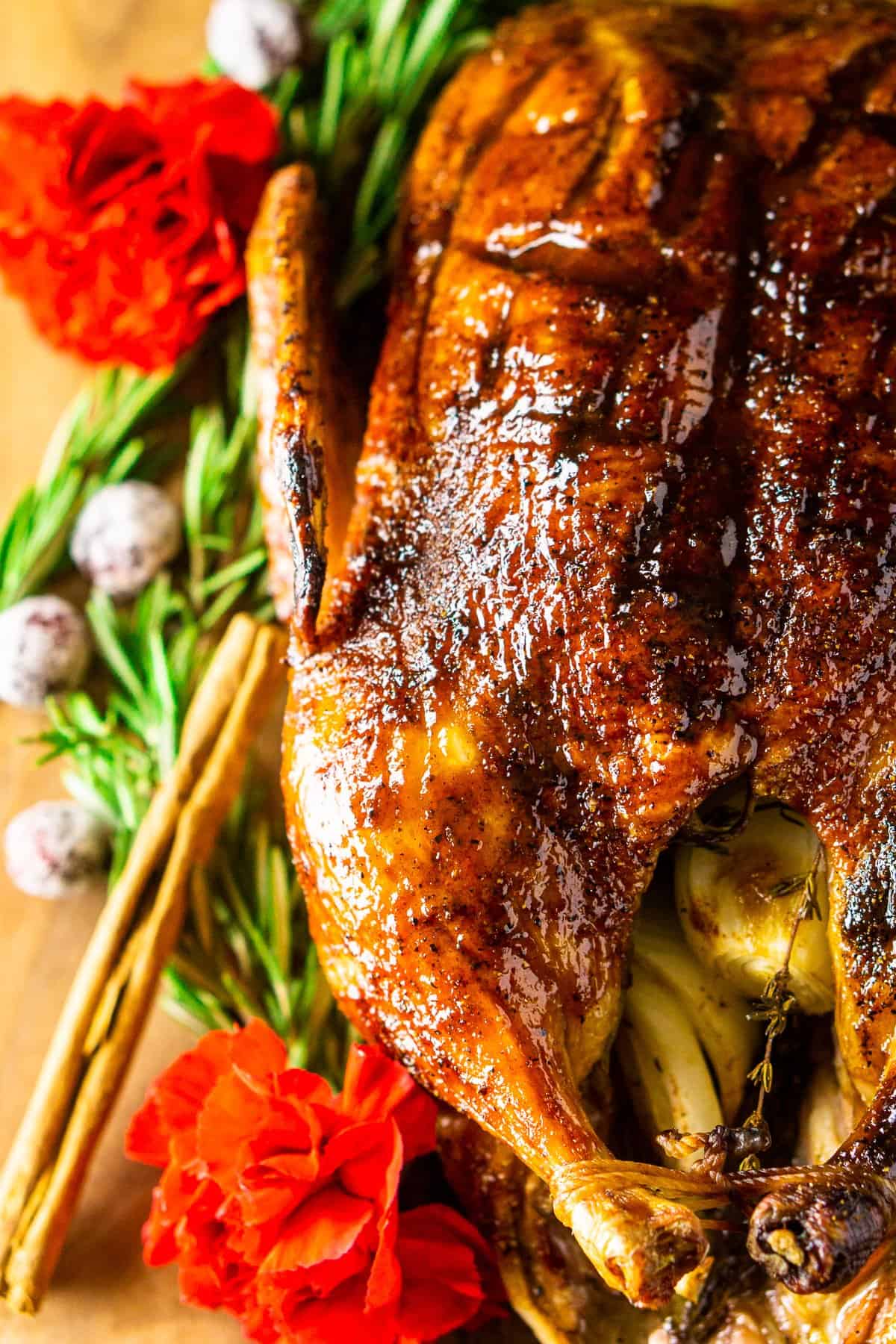 The roasted holiday duck on a bed of rosemary with cinnamon sticks and flowers to the side.