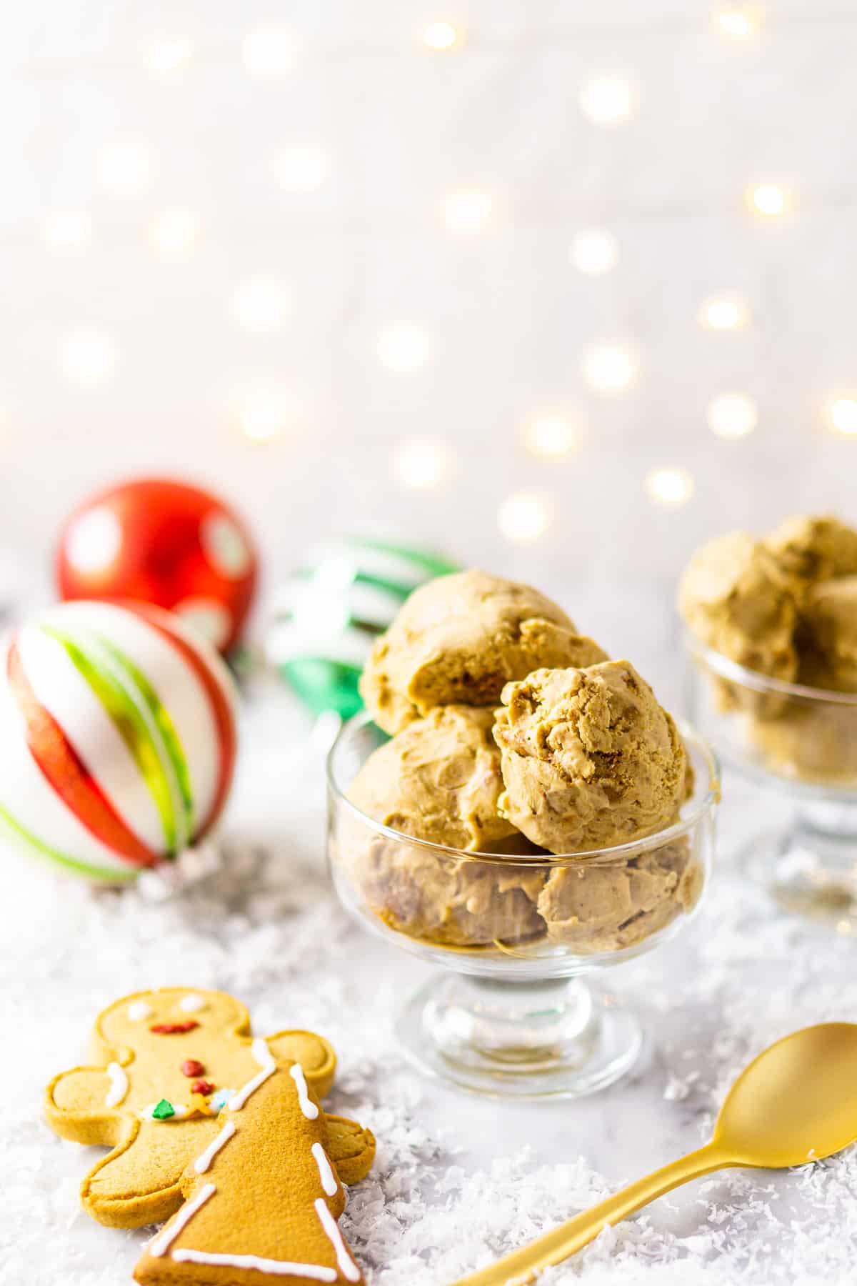 The gingerbread ice cream with a spoon to the side and gingerbread cookies on the other side with lights in the background.