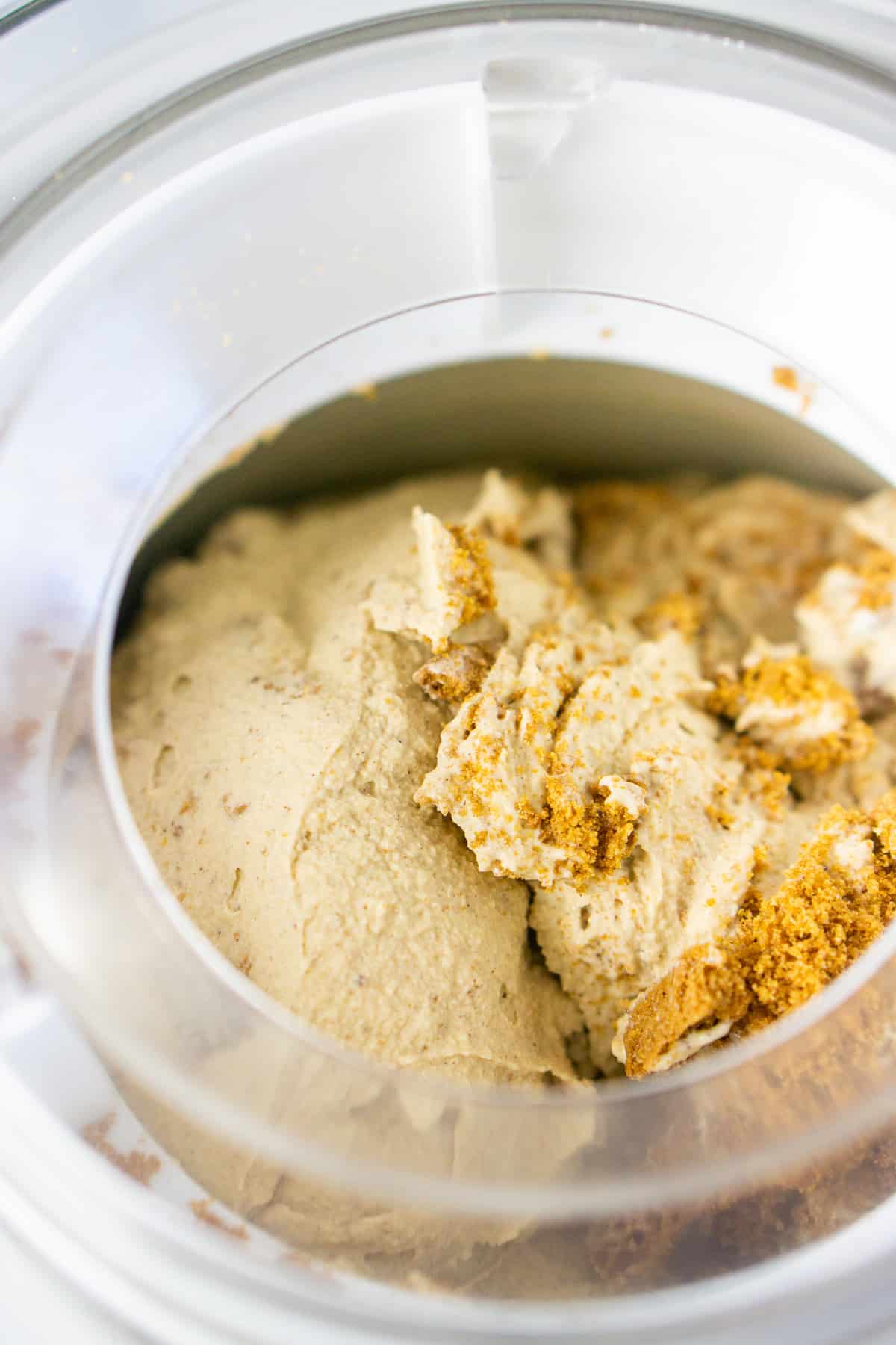 The ice cream in the ice cream maker with crushed ginger snaps being churned into the mixture.