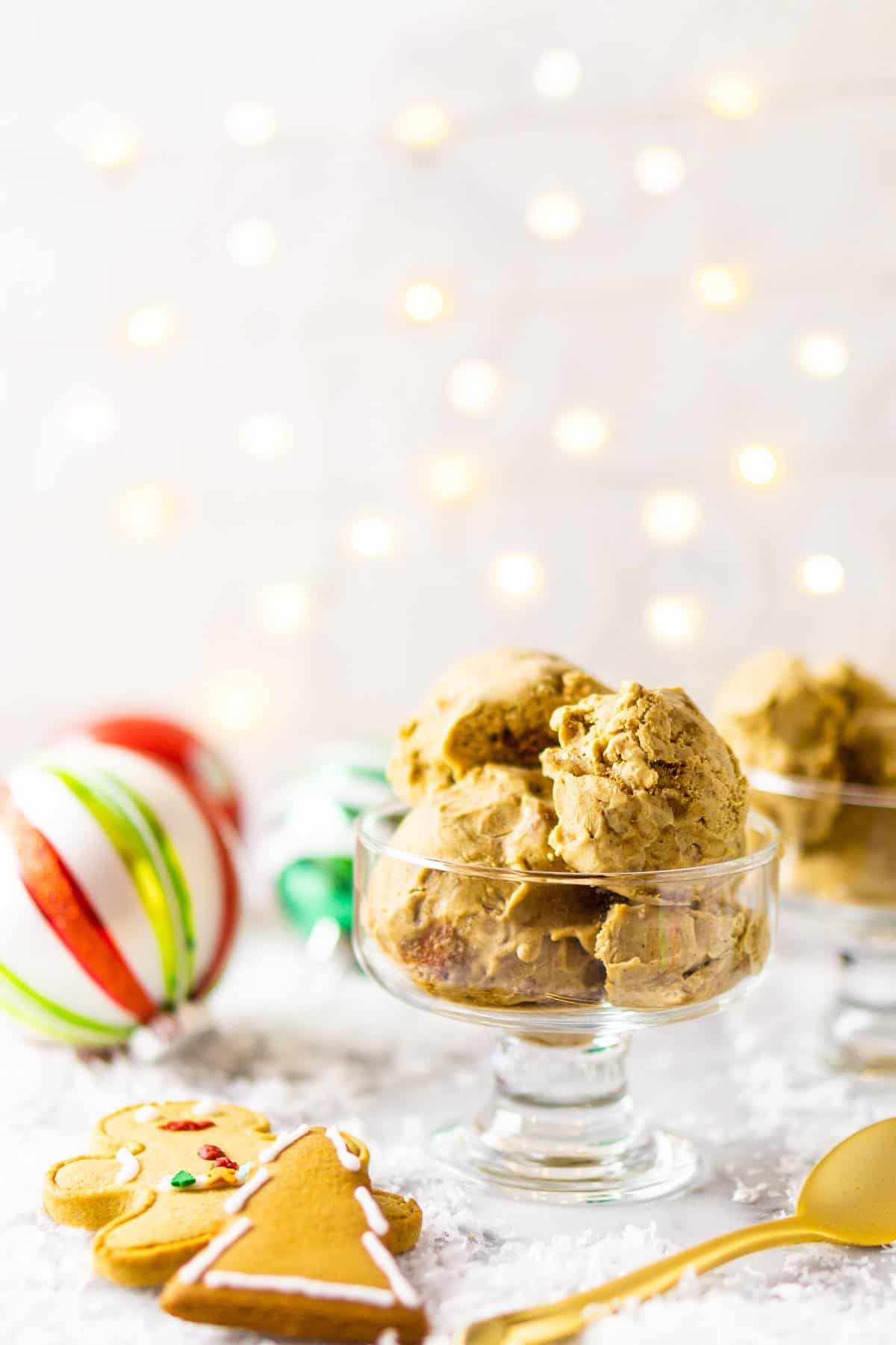 A bowl of gingerbread ice cream with lights in the background, a spoon to the side and Christmas decor around it.