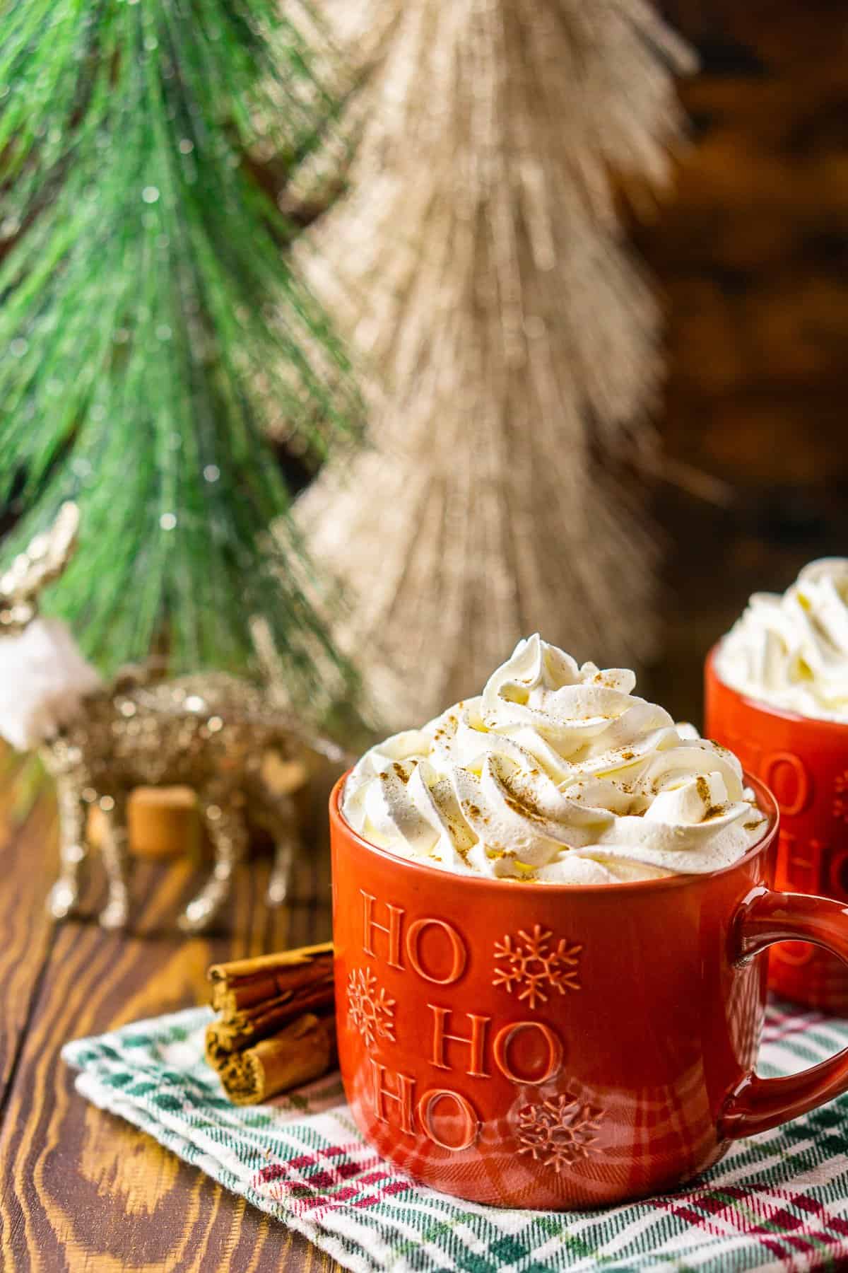 Two mugs of this homemade gingerbread latte with cinnamon sticks to the side and Christmas decor in the background.