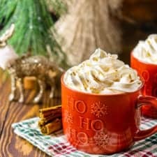 Two mugs of this homemade gingerbread latte with cinnamon sticks to the side and Christmas decor in the background.