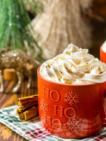 Two mugs of this homemade gingerbread latte with cinnamon sticks to the side and Christmas decor in the background.