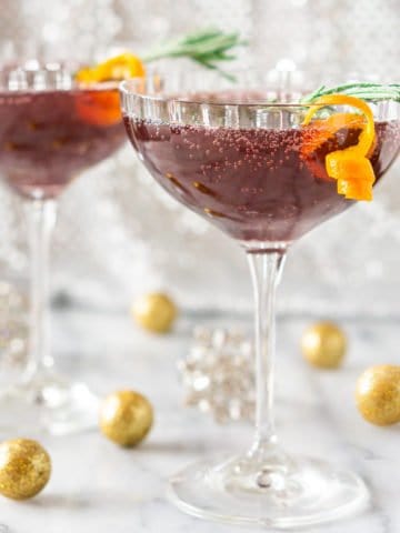 A sparkling pomegranate martini on a marble board with glittery balls around it.
