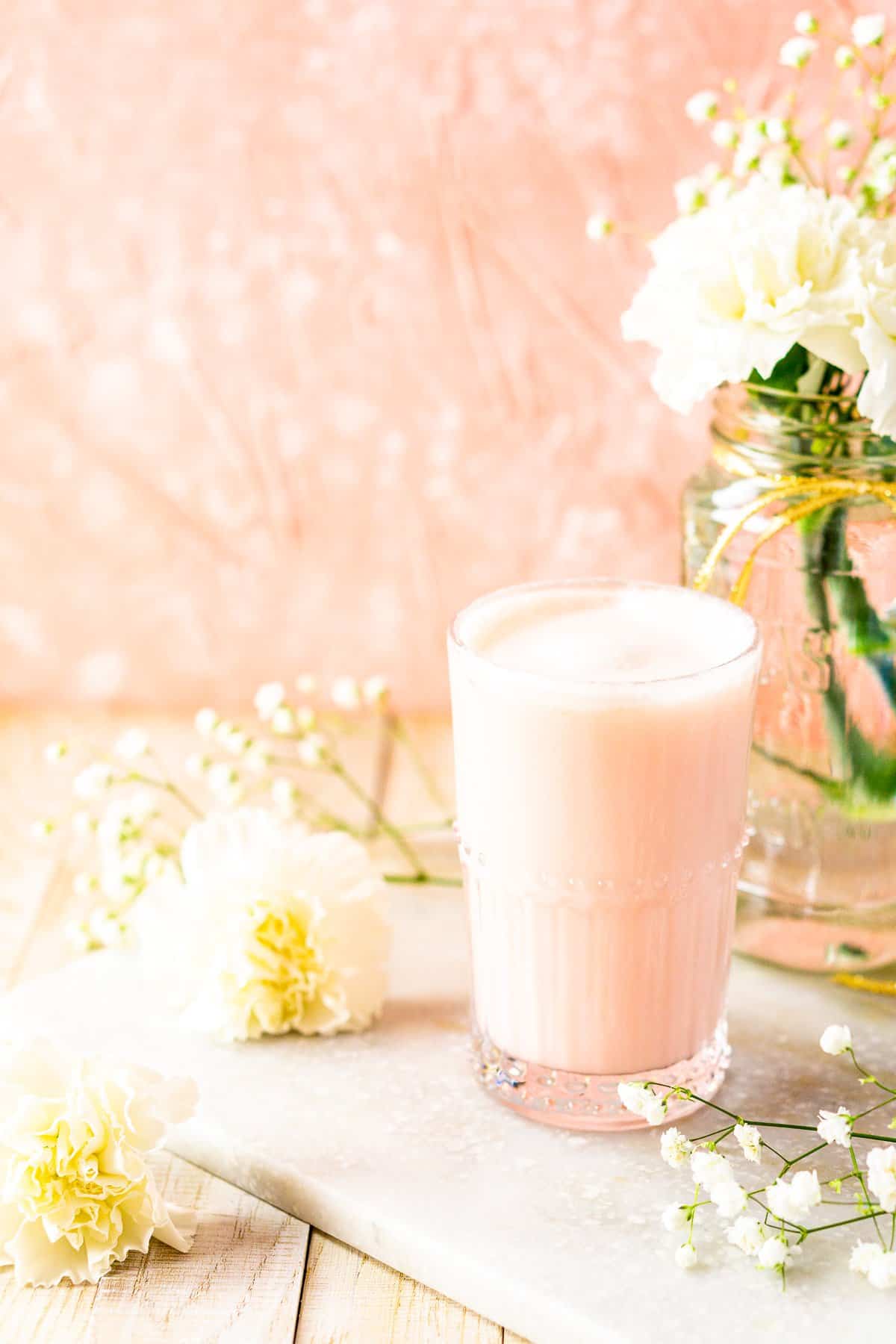 A blood orange cocktail on a white marble board with flowers against a pink background.