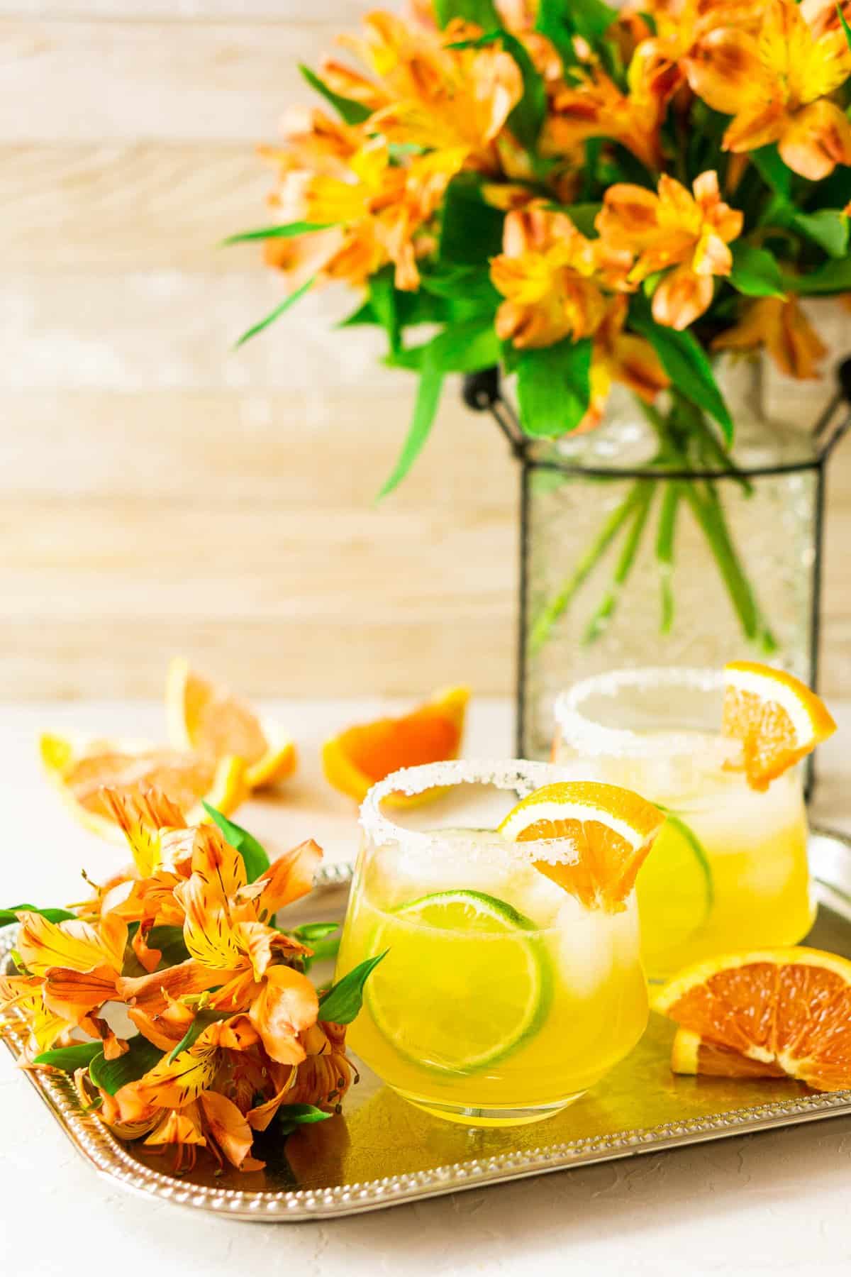 Two cara cara margaritas on a silver platter with orange flowers and Cara Cara slices to the side.