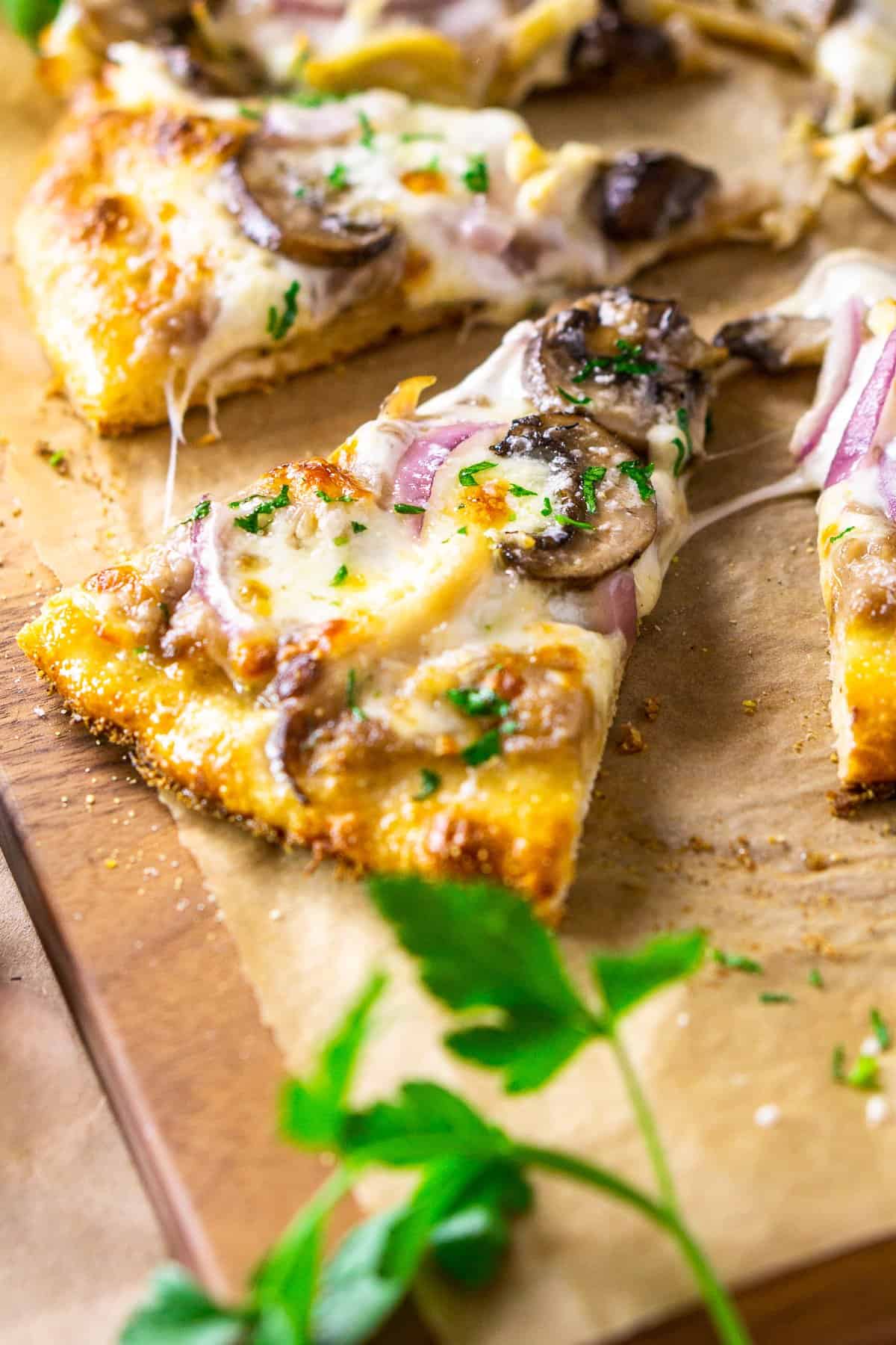 A close-up of a slice of coq au vin pizza with fresh parsley framing the pizza on a cutting board.
