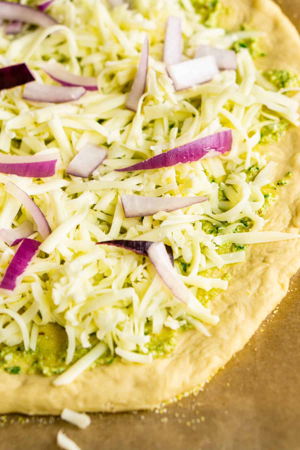 The pizza topped with cheese, pesto and red onions before baking.