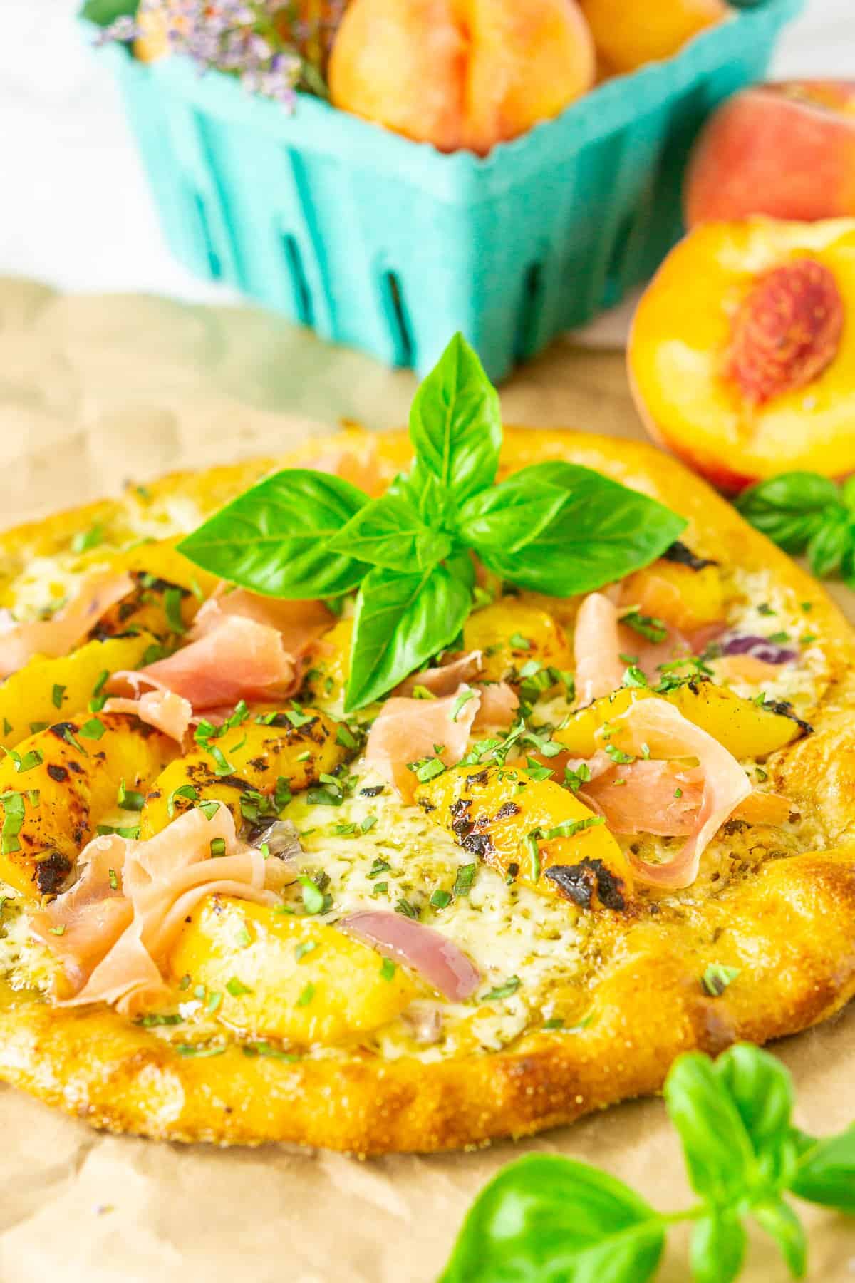 A whole grilled peach pizza with peach halves and basil.