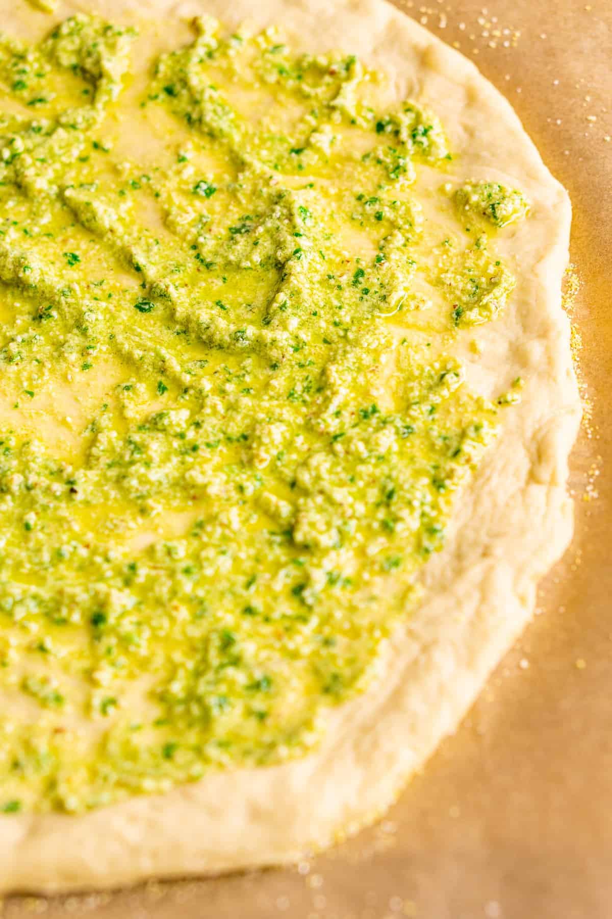 Pizza dough on cornmeal-dusted parchment paper with pesto on top.