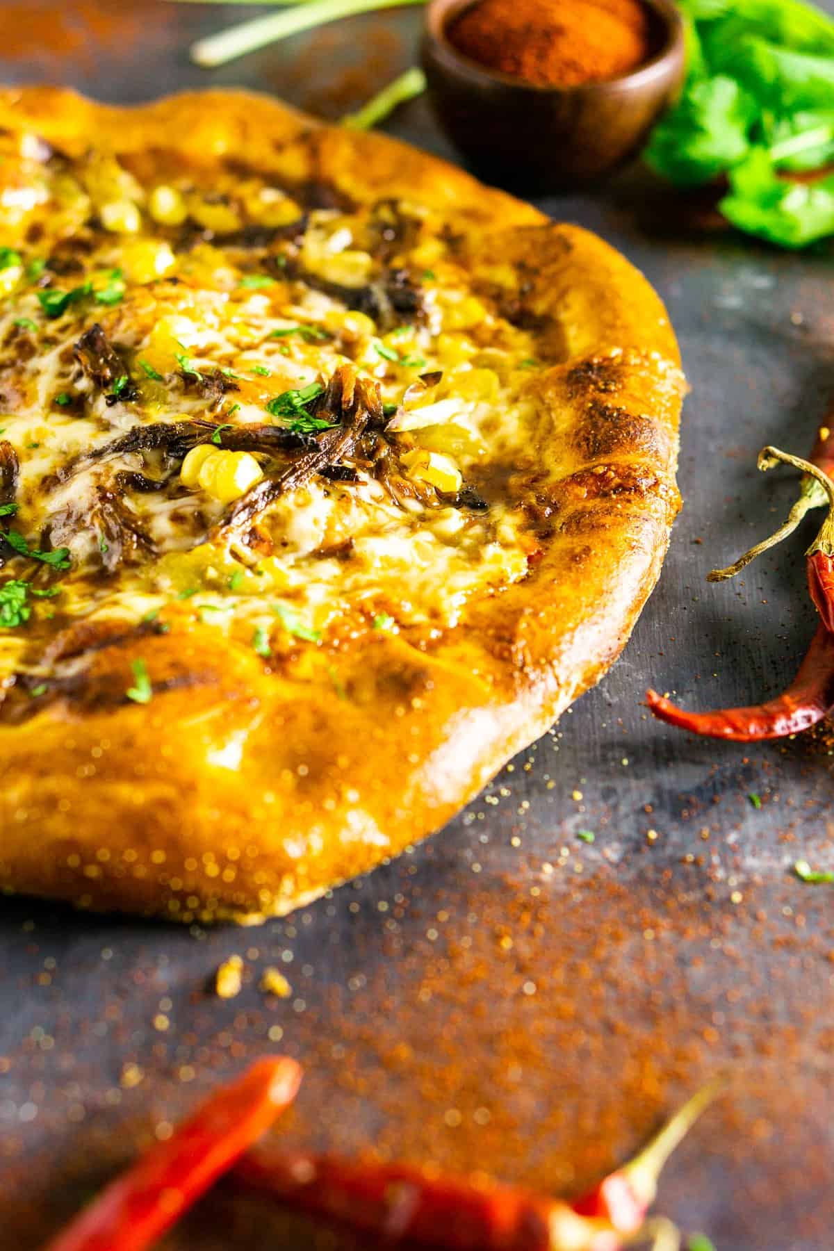 The Mexican beef pizza on a slate board with dried chile peppers.