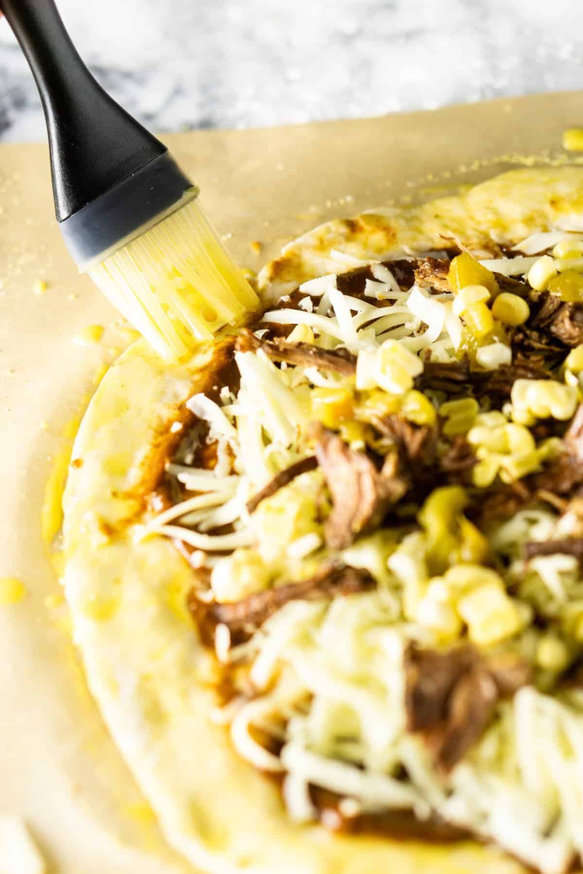 Brushing the Mexican beef pizza with an egg wash on a floured pastry board.