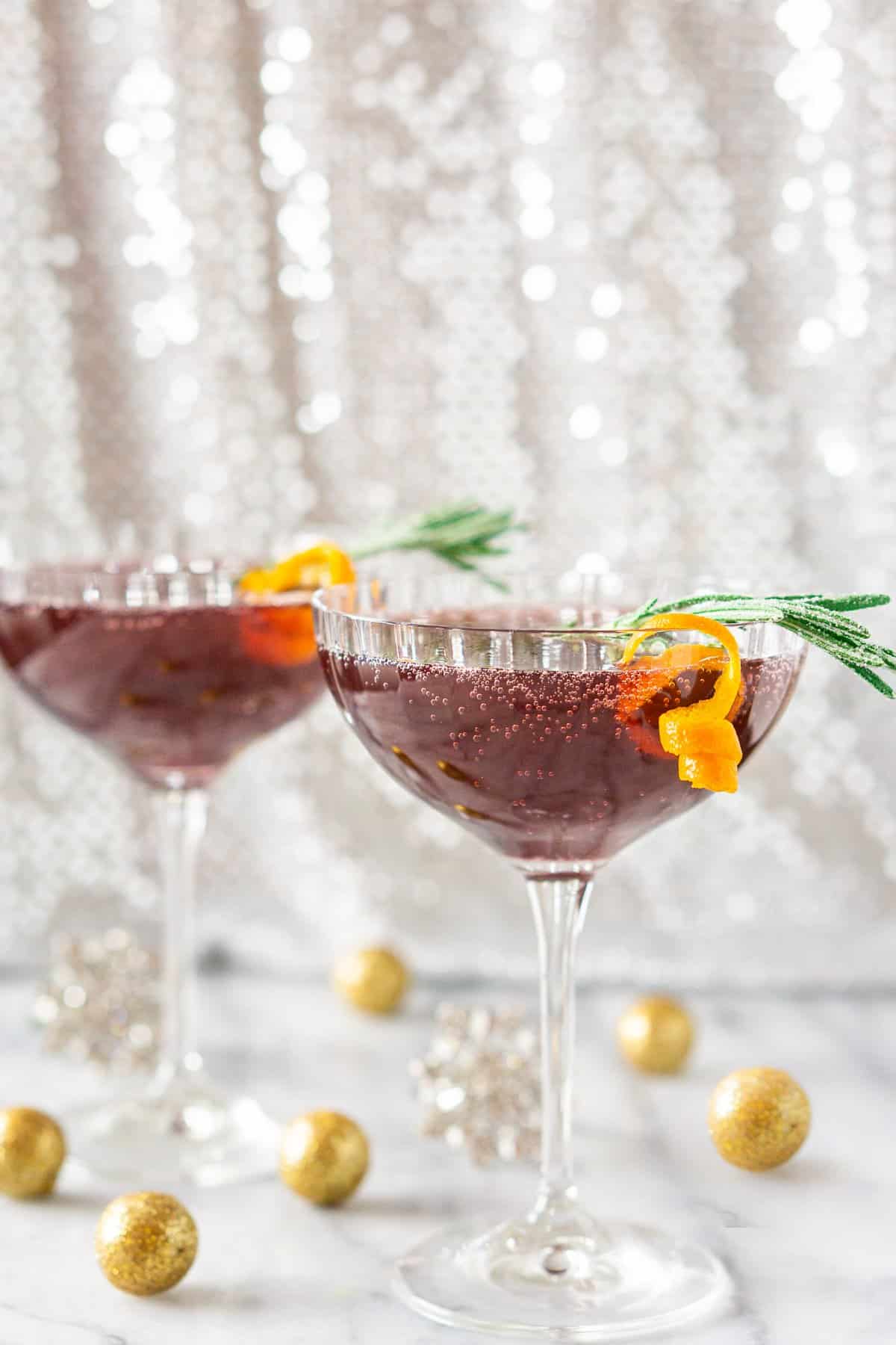 A sparkling pomegranate martini on a marble board with glittery balls around it.