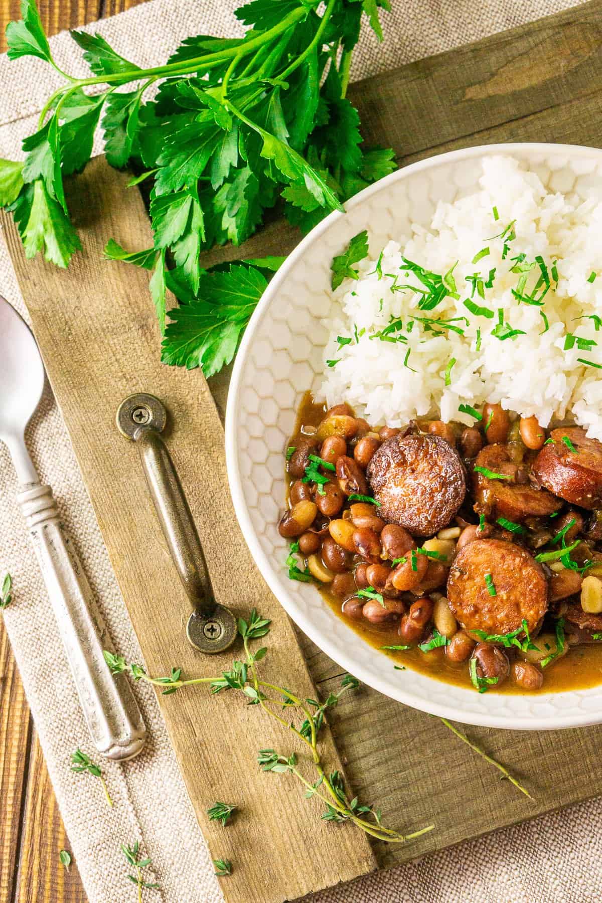 A bowl of Instant Pot red beans and rice on a wooden tray with a bunch of parsley in the background and a spoon to the side.