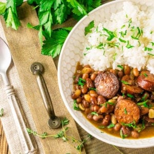 A bowl of Instant Pot red beans and rice on a wooden tray with a bunch of parsley in the background and a spoon to the side.