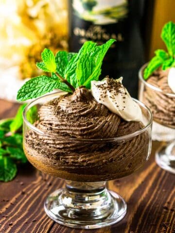 A cup of Baileys mousse with a bottle of Irish cream behind it with a sprig of mint to the side.