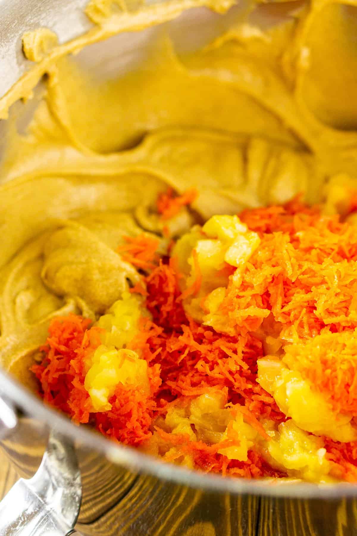 Stirring in the pineapple, carrots and coconut into the batter in a mixing bowl.