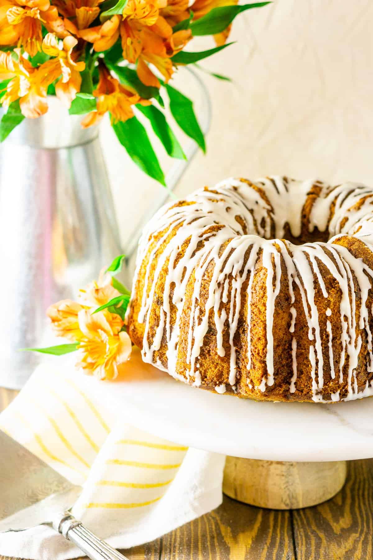 Looking straight on at the carrot cake with flowers on the cake stand and in the background.