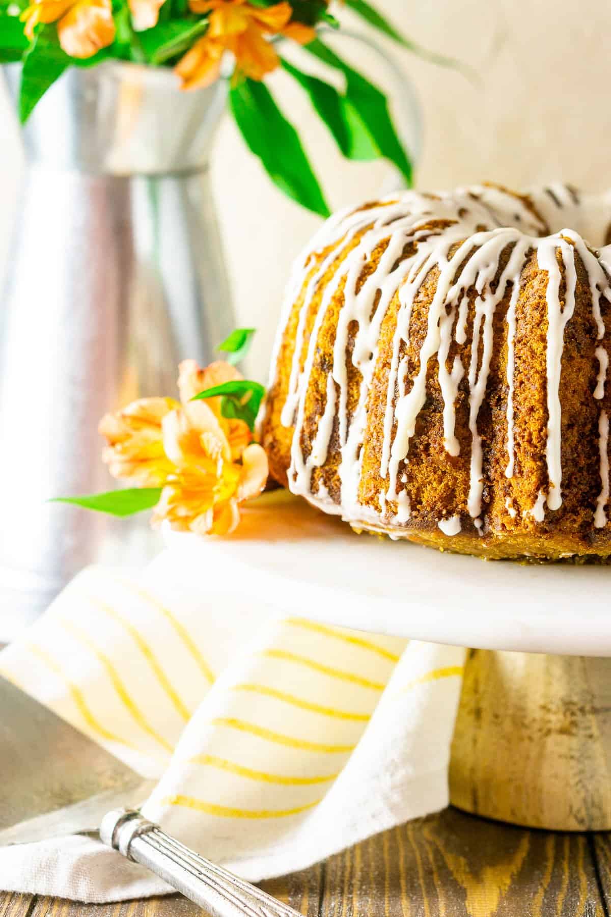 The carrot pound cake on a white marble cake stand with orange flowers.